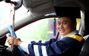 man in graduation robe and hat in car smiling